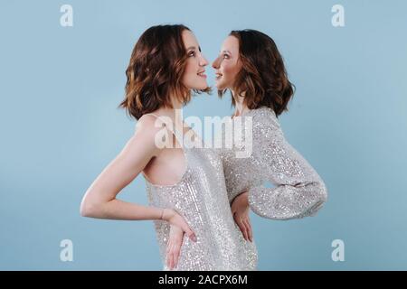 Two twin sisters in shiny evening dresses, looking in different directions Stock Photo