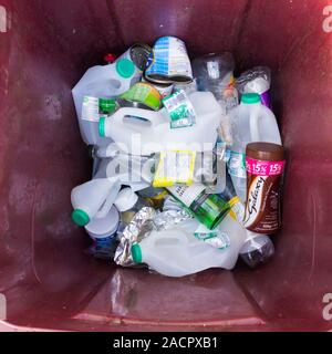 Recyclable houshold waste: plastic bottles, metal tin cans  and glass  bottle domestic recycling waste in a maroon wheelie bin. Stock Photo