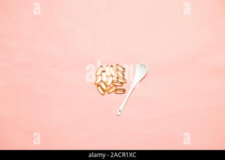 Top view of assorted multi-colored medical capsules, tablets and a ceramic spoon on a pink background. Stock Photo