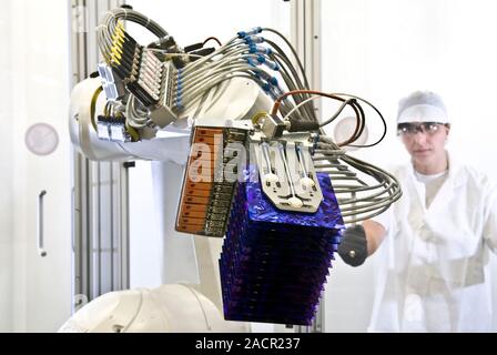 Manufacturing solar panels. Worker operating a robot used to handle the delicate solar cells (photovoltaic cells, blue) at a factory that manufactures Stock Photo