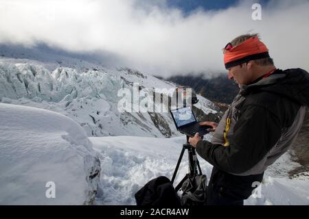 Glaciology research. Researcher using a laptop computer to access and study photography of glacier movements. This is the Argentiere Glacier in the Fr Stock Photo