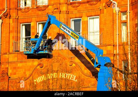 Two men on a hydraulic platform working on the front of the Midland Hotel in bright late afternoon winter sunshine,Manchester,UK Stock Photo