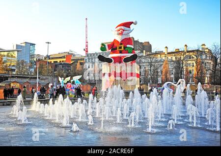 Giant santa model sat on top of gift wrapped present behind fountain in Piccadilly Gardens,Manchester UK Stock Photo