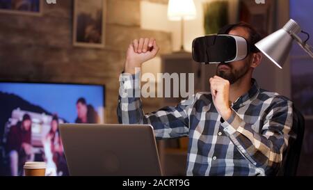 Bearded businessman using virtual reality goggles in home office. Businessman working late. Stock Photo