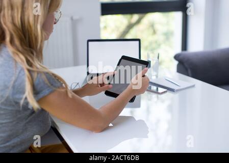 A young woman holding a mock up tablet with the mock up laptop in the background. Young woman using tablet with white blank screen Stock Photo