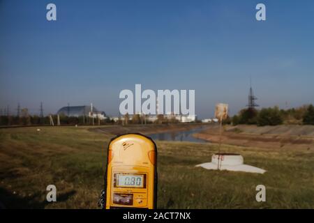 A dosimeter is held with the New Safe Confinement (the 'Sarcophagus') of the Chernobyl reactor seen in the distance. Pripyat, Ukraine. Stock Photo