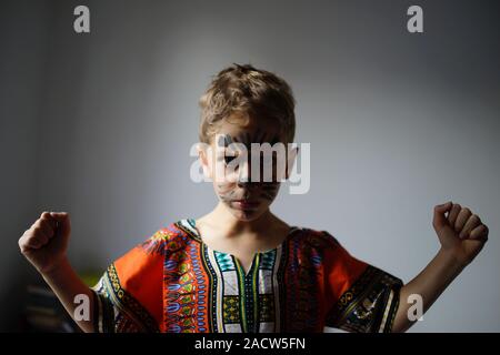 Boy with painted face and raised fists, raised wearing traditional African Dashiki shirt Stock Photo