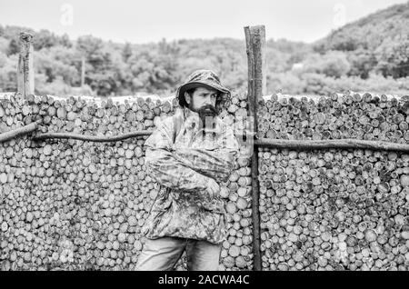 bearded man in hiking camp. mature hipster with beard in military jacket. Hunter man. Hunting season. Poacher. soldier at firewood stocks fence. military uniform. brutal male. Illegal business. Stock Photo