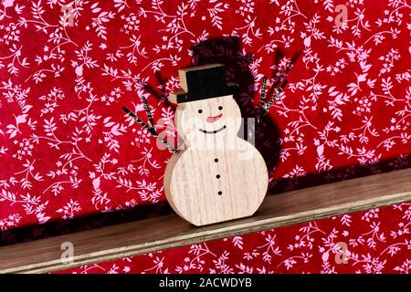 a funny wooden snowman, with a red nose and wearing a hat, on a wooden shelf against a floral-patterned wallpapered wall Stock Photo