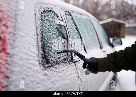 Cleaning the side car windows of snow with ice scraper before the trip. Man removes ice from car windows. Male hand cleans car with special tool at Stock Photo