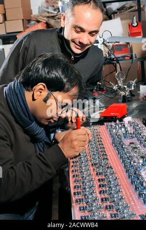 Wireless sensor network production. Engineers working on the production of circuit boards for a wireless sensor network, with the engineer at left usi Stock Photo