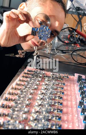 Wireless sensor network production. Engineer using a magnifying glass to examine the quality of circuit boards made for a wireless sensor network. He Stock Photo