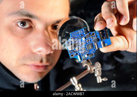Wireless sensor network production. Engineer using a magnifying glass to examine the quality of circuit boards made for a wireless sensor network. He Stock Photo