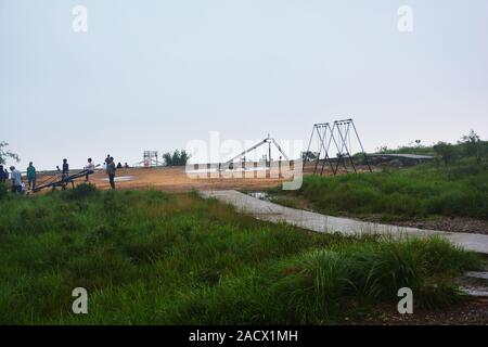 Long shot of the playing area of the children with slide and green grasses and trees of the Cherrapunjee Eco Park with blue sky and pathway, selective Stock Photo