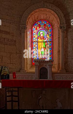stained glass window, behind side altar, colorful, religious art, bishop, votive light burning, St. Martin de Chapaize Catholic church, Saone-et-Loire Stock Photo