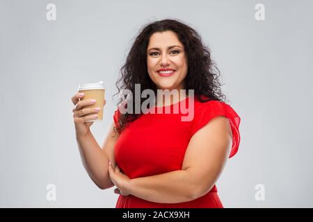 people and drinks concept - portrait of happy woman in red dress holding takeaway coffee cup over grey background Stock Photo
