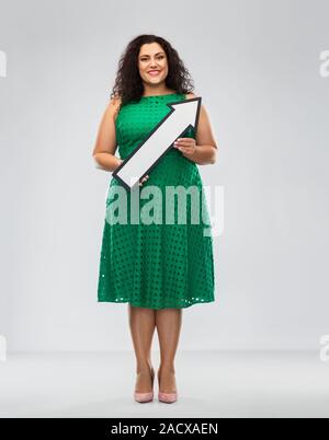 people, direction and communication concept - happy woman in green dress holding big white thick arrow showing to north east over grey background Stock Photo