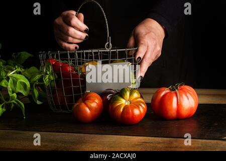 Woman putting differents tomatoes in a wire basket Stock Photo