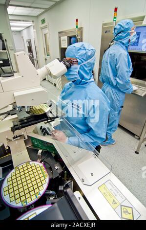 Silicon wafer research. Researchers working in a clean room to develop advanced silicon wafer technology. In electronics, a silicon wafer (round objec Stock Photo