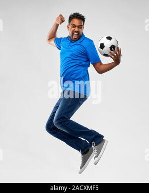 sport, leisure games and people concept - happy indian man or football fan with soccer ball jumping over grey background Stock Photo