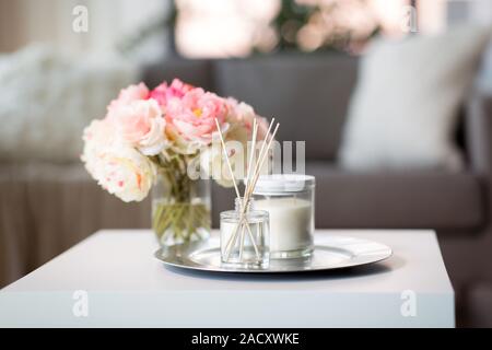 decoration, hygge and cosiness concept - aroma reed diffuser, candle and flower bunch on wooden table Stock Photo