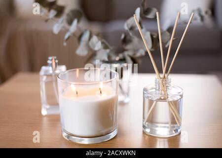 decoration, hygge and aromatherapy concept - aroma reed diffuser, burning candle and perfume on table at home Stock Photo