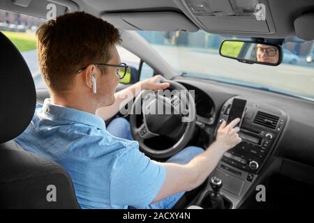 transport, vehicle and people concept - man or driver with wireless earphones driving car and using gps navigator on smartphone Stock Photo