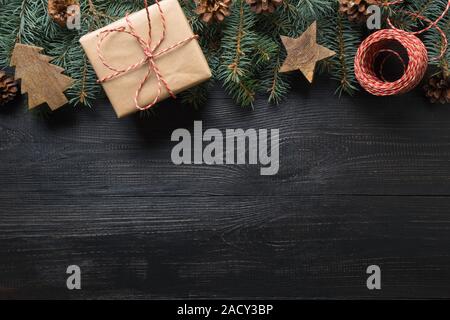 Christmas frame of fir branches, gift and wooden toys on dark wooden board. Top view. Space for text. Zero Waste Holiday. Eco friendly. Stock Photo