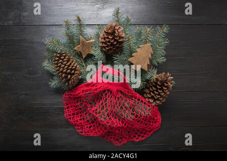 Christmas zero waste holiday. Coniferous fir tree branches in red cotton eco bag on black wooden board. Eco friendly Xmas. Stock Photo