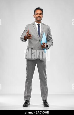 business, office worker and people concept - smiling indian businessman with folder stretching hand out for handshake over grey background Stock Photo