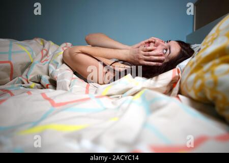 Young woman lying in bed suffering with insomnia  Noisy neighbour, stress, alarm sound, prevent from sleep concept Stock Photo