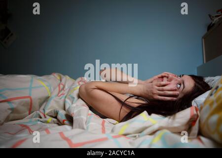 Young woman lying in bed suffering with insomnia  Noisy neighbour, stress, alarm sound, prevent from sleep concept Stock Photo