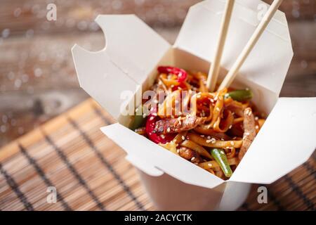 Noodles with pork and vegetables in take-out box on wooden table Stock Photo