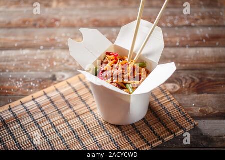 Noodles with pork and vegetables in take-out box on wooden table Stock Photo