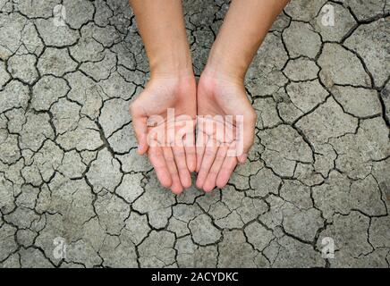 Asian woman's hand On dry, cracked soil or soil during the dry season Stock Photo