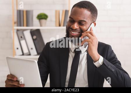 Cheerful businessman using tablet while talking by phone Stock Photo