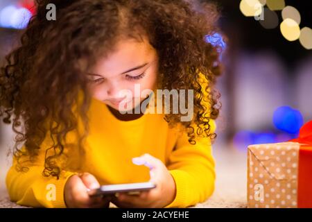 Little african girl playing on cellphone ignoring Christmas gift Stock Photo