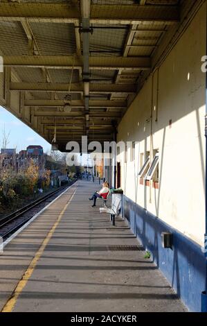 A middle aged woman sitting alone on an empty railway station platform waiting for a train Kingston station greater London Surrey England UK Stock Photo