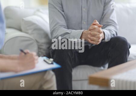 Psychologist taking notes during psychotherapy session with man Stock Photo