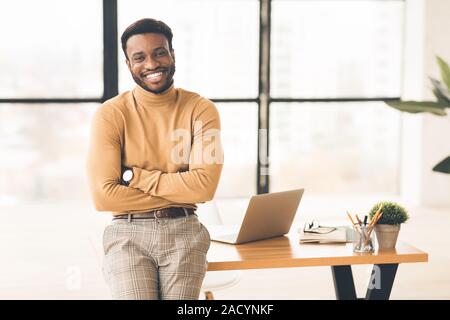 Successful black man sitting on desk at office Stock Photo