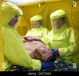 Major emergency decontamination training. Emergency workers in sealed positive pressure protective suits using cleaning equipment on a casualty with s Stock Photo