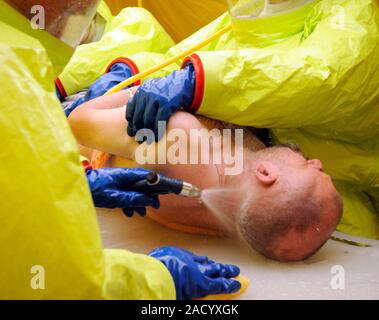 Major emergency decontamination training. Emergency workers in sealed positive pressure protective suits using cleaning equipment on a casualty with s Stock Photo