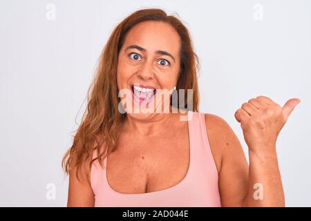 Middle age mature woman standing over white isolated background pointing and showing with thumb up to the side with happy face smiling Stock Photo