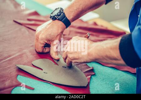 Close up hands of an experienced shoemaker measuring and cutting leather in a workshop. Selective focus Stock Photo
