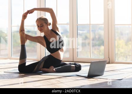 Athletic young woman stretching at home, using laptop Stock Photo