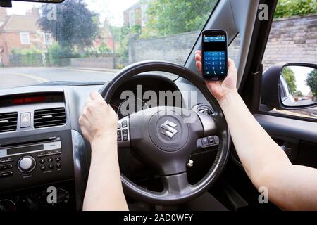 Phone use while driving. Driver's view of a driver with one hand on the car steering wheel and the other hand using a mobile phone. Stock Photo