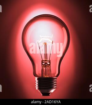 View of an incandescent light bulb. The bulb glows because of a current passing through a thin, coiled tungsten wire. The current heats the wire, maki Stock Photo