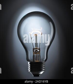 View of an incandescent light bulb. The bulb glows because of a current passing through a thin, coiled tungsten wire. The current heats the wire, maki Stock Photo
