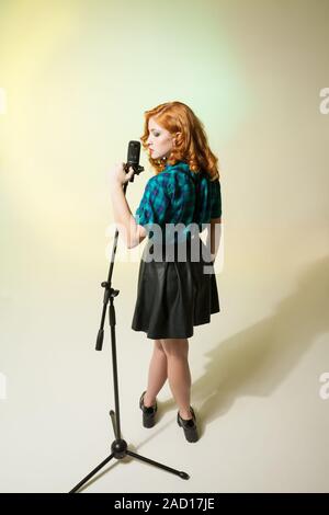 Stylish singer with curly red hair holding mic Stock Photo