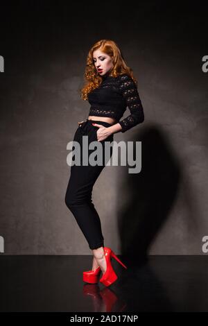 Red-haired woman posing against of black wall in light Stock Photo